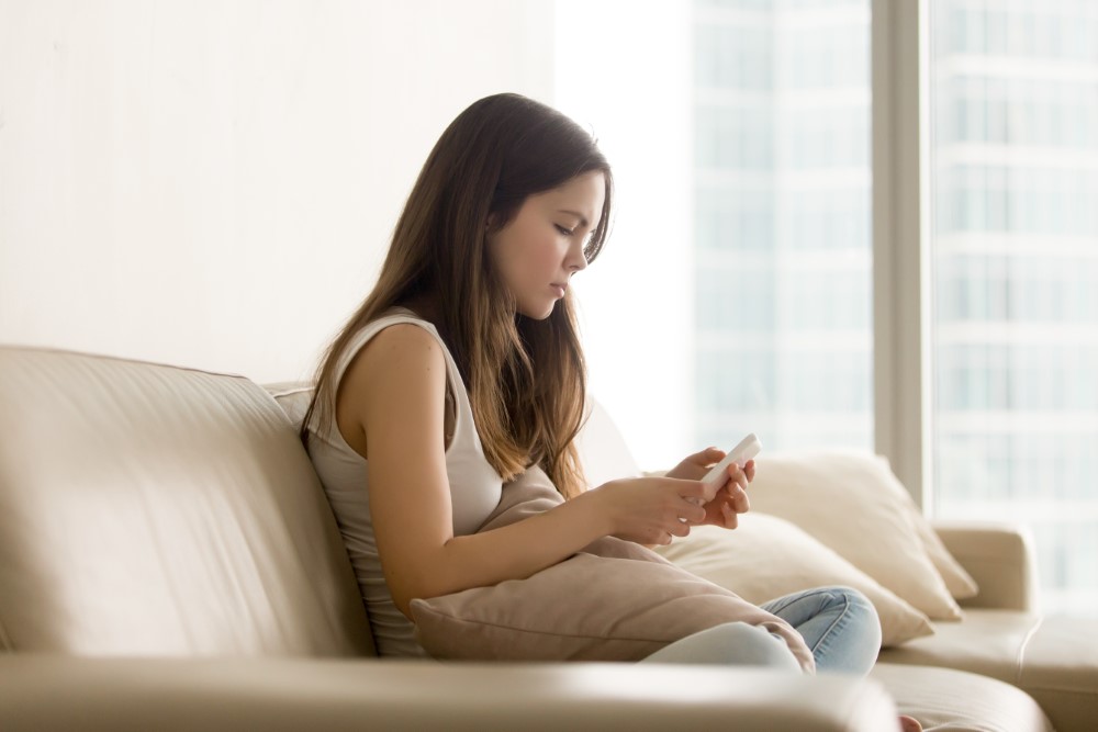 sad teen girl using phone while sitting sofa